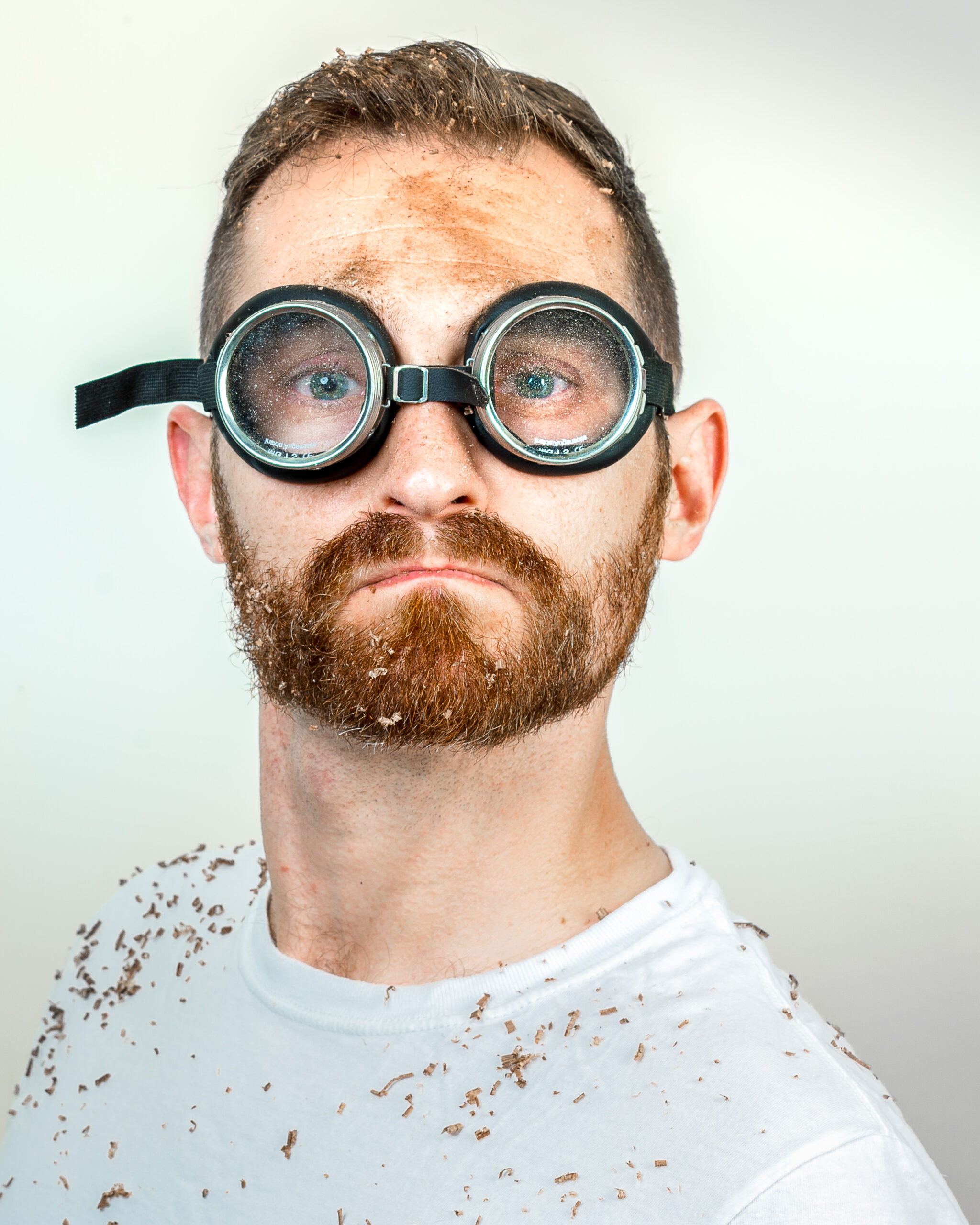 A man covered in sawdust wearing safety goggles.